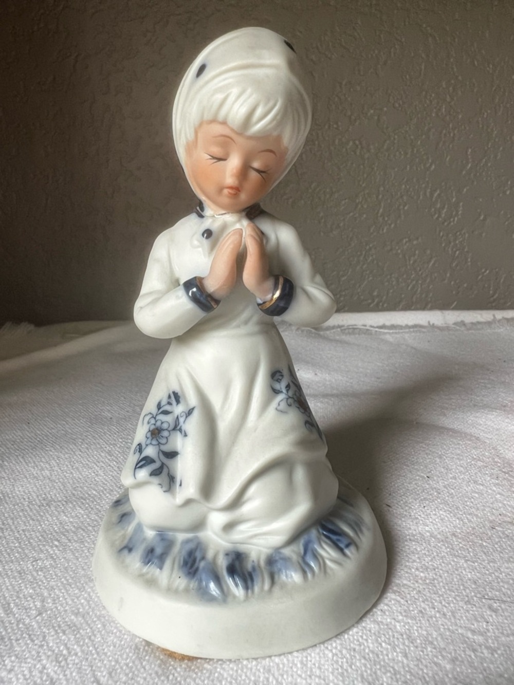vintage porcelain figurine depicts a praying girl with a blue floral